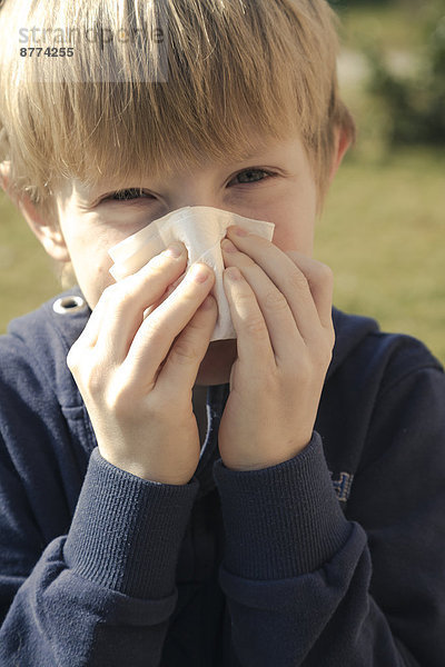 Porträt eines Jungen  der sich mit einem Taschentuch die Nase bläst.