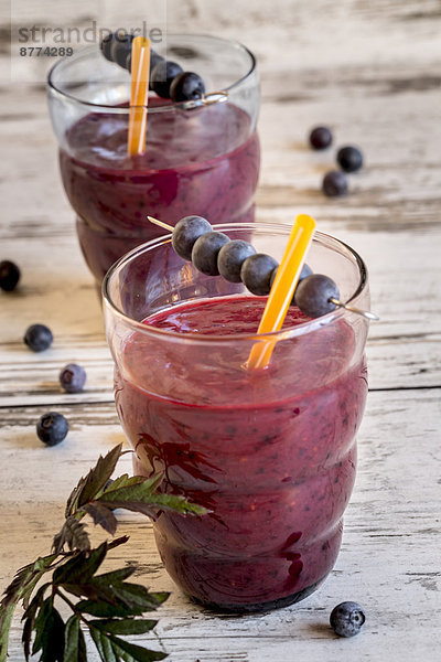 Two glasses of wild berry smoothie and blueberries on wooden table