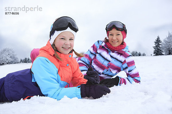Deutschland  Masserberg  Mutter und Tochter im Schnee liegend  glücklich lächelnd