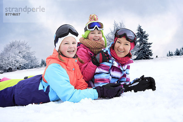 Deutschland  Masserberg  Mutter und Töchter im Schnee liegend  glücklich lächelnd
