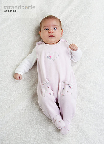 Weibliches Baby mit rosa Strampler auf weißem Stoff liegend