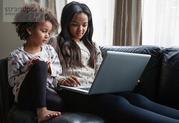 Zwei Schwestern auf dem Sofa sitzend mit Laptop