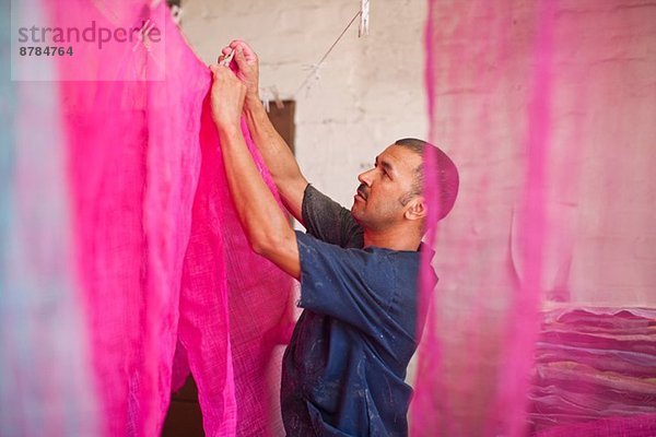 Mann beim Aufhängen von gefärbtem Stoff in der traditionellen Müllerwerkstatt