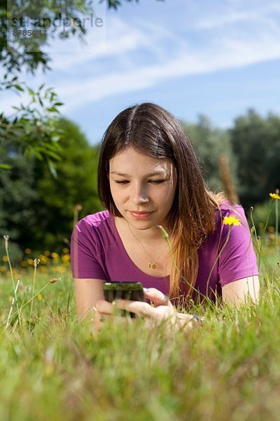 Teenager-Mädchen liegt im Park und schaut auf das Handy.
