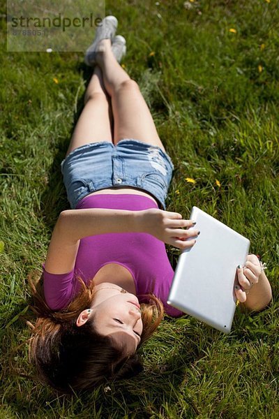 Teenagermädchen entspannt im Park beim Betrachten des digitalen Tabletts