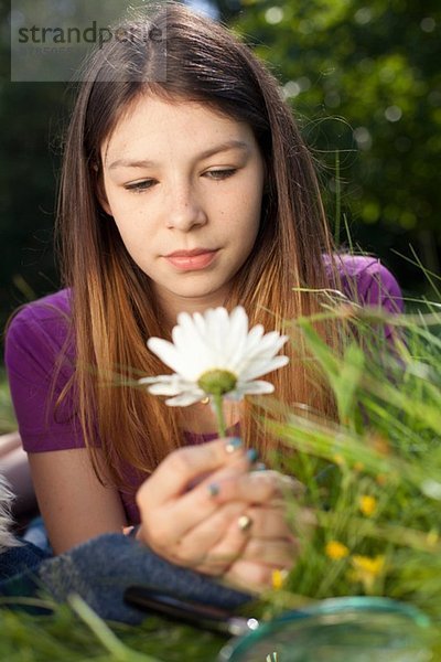 Teenager-Mädchen im Gras liegend mit Blick auf ein Gänseblümchen
