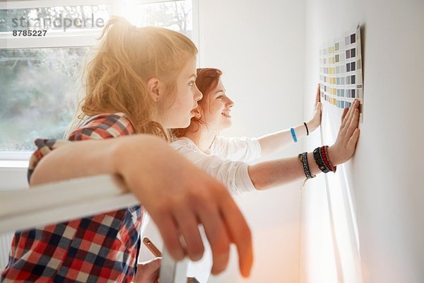 Teenager-Schwestern mit Farbmuster an der Wand