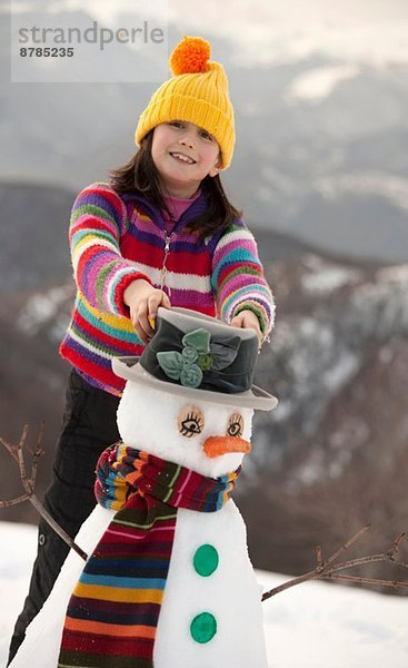 Teenagermädchen platziert Hut auf Schneemann