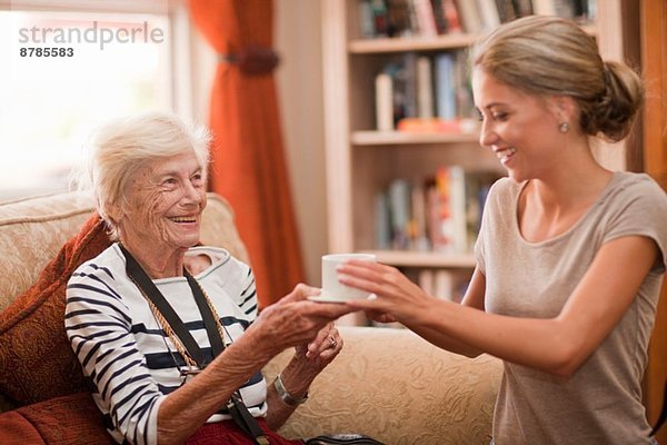 Pflegeassistentin bei der Übergabe der Kaffeetasse an die Seniorin