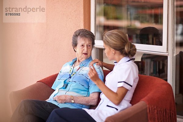 Betreuerin im Gespräch mit Seniorin auf dem Sofa