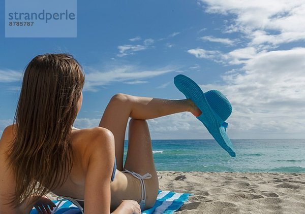 Junge Frau entspannt am Strand mit blauem Sonnenhut