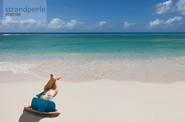 Junge Frau entspannt am Strand mit blauem Sonnenhut