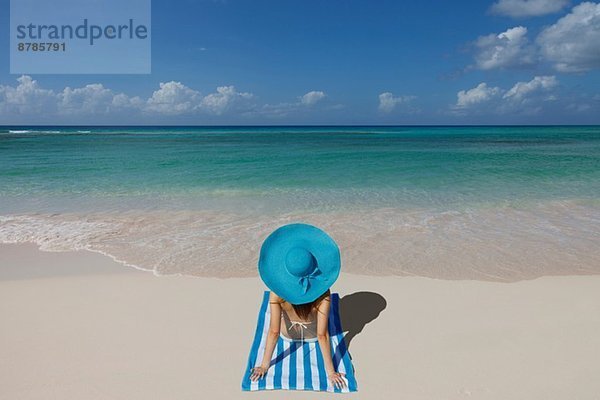 Junge Frau entspannt am Strand mit blauem Sonnenhut