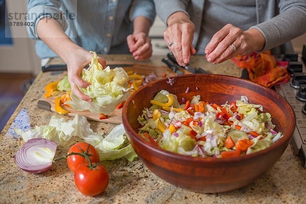 Seniorin und Enkelin hacken Gemüse für Salat