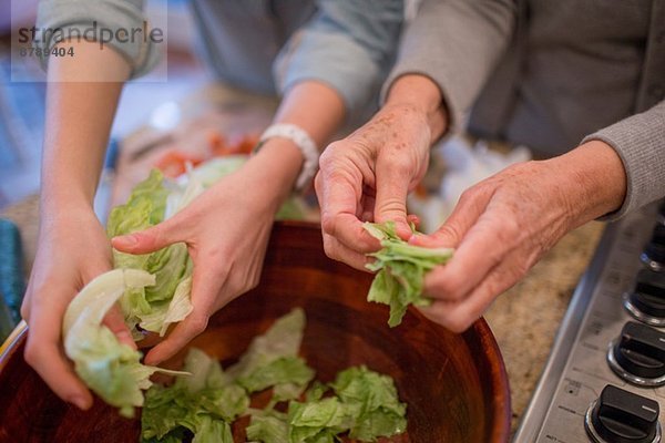 Seniorin und Enkelin bereiten Salat für Salat zu.