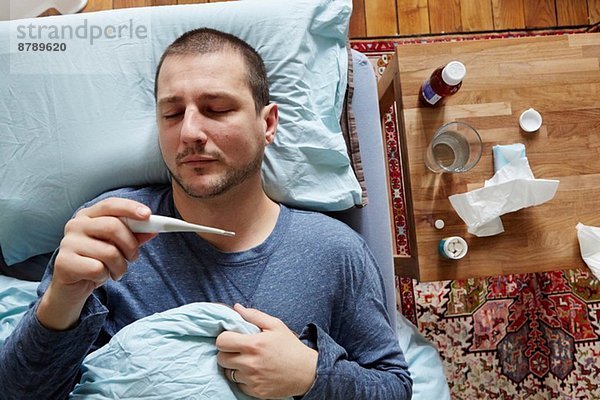 Mittlerer erwachsener Mann im Bett liegend mit Blick auf den Thermometerstand