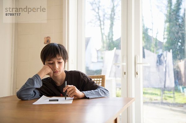 Junge am Tisch sitzend  Stift an Papier halten