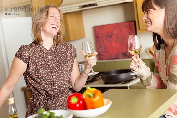 Mittlere erwachsene Freundinnen trinken Wein und lachen in der Küche