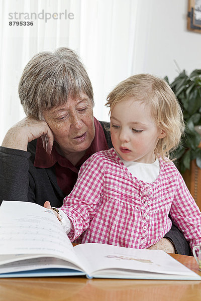 Großmutter liest der 3-jährigen Enkeltochter aus einem Buch vor