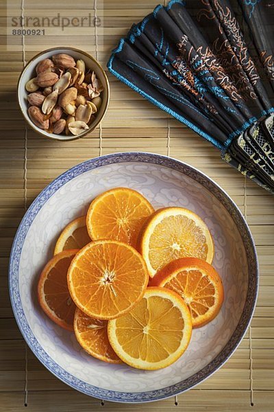 Orangenscheiben auf Teller  daneben Schälchen mit Erdnüssen