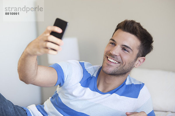 Junger Mann liegt auf dem Bett und nimmt Selfie mit dem Smartphone.