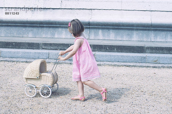 Kleines Mädchen schiebt Miniatur-Kinderwagen