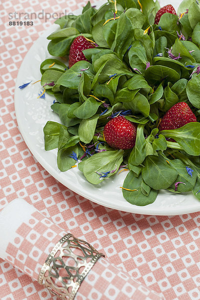 Feldsalat mit Erdbeeren und Blütenblättern angerichtet auf einem Teller