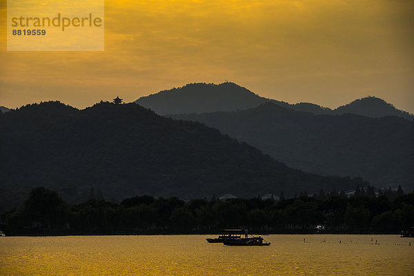 Hügellandschaft am Westsee bei Sonnenuntergang mit Fischerboot  Xihu  Hangzhou  Provinz Zhejiang  China