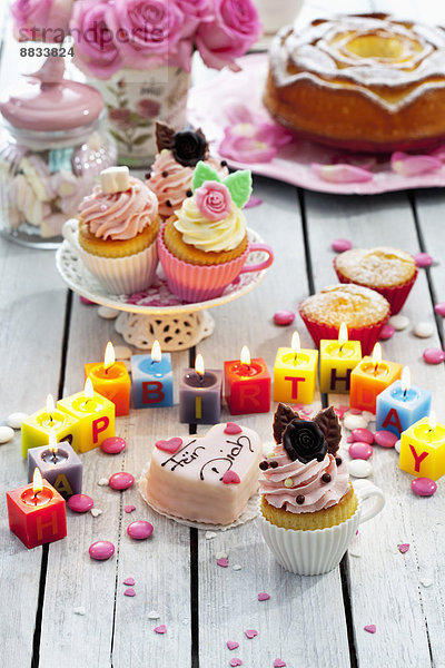 Muffins  Geburtstagskuchen  Tassenkuchen  Rosen  angezündete Geburtstagskerzen und Backdekor auf dem Tisch