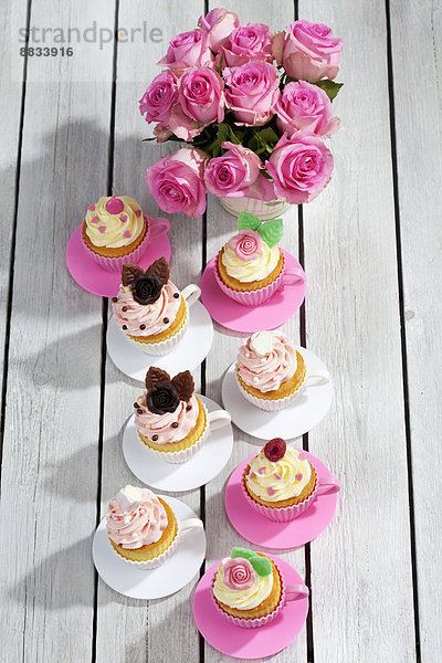 Backformen wie Tassen mit dekorierten Muffins und Rosen auf Holztisch  erhöhte Ansicht