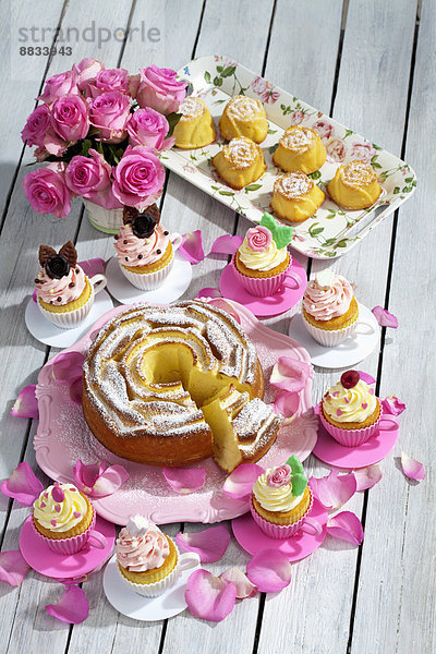 Geburtstagstorte  Törtchen  Muffins und Blumenvase aus rosa Rosen auf Holztisch