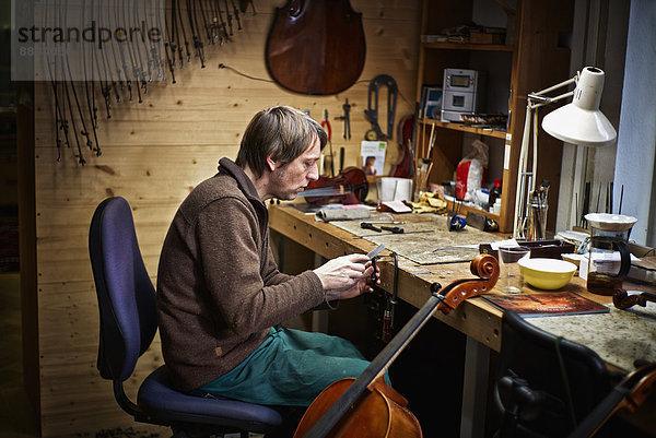 Geigenbauer in seiner Werkstatt beim Einordnen eines Cello-Mechanismus