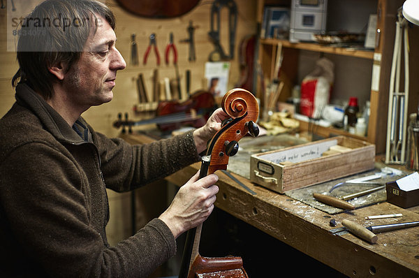 Geigenbauer in seiner Werkstatt beim Einstellen einer Cello-Mechanik
