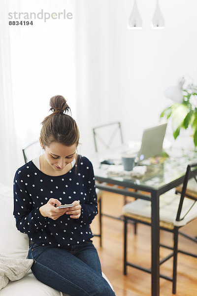 Junge Frau schreibt SMS mit Smartphone zu Hause