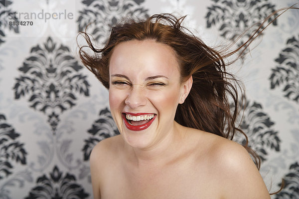 Porträt einer lachenden jungen Frau vor karierter Tapete