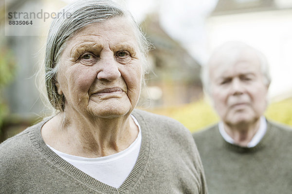 Porträt einer älteren Frau mit Mann im Hintergrund