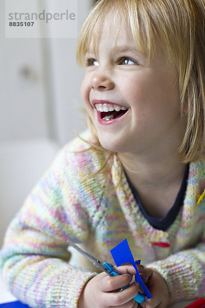 Porträt des lächelnden Mädchens mit Schere und farbigem Papier