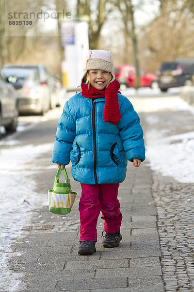 Kleines Mädchen mit Tasche auf dem Bürgersteig