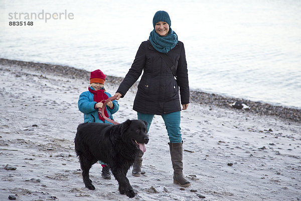 Deutschland  Schleswig-Holstein  Kiel  Mutter und Tochter gehen mit Labrador am Strand entlang.
