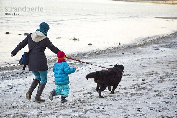 Deutschland  Schleswig-Holstein  Kiel  Mutter und Tochter gehen mit Labrador am Strand entlang.