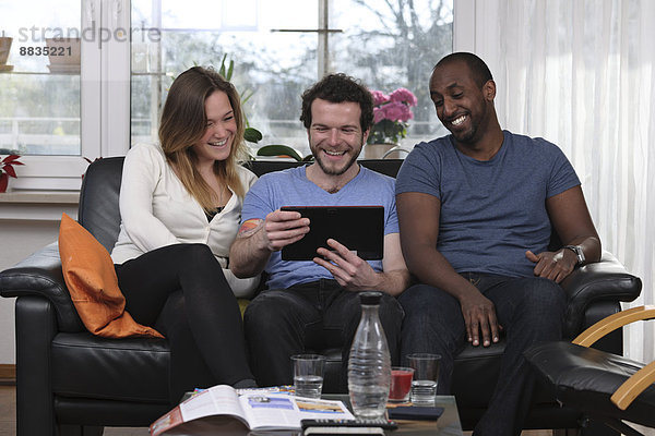 Drei Freunde haben Spaß mit dem Tablet-Computer zu Hause
