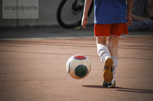 Junge tritt Fußball auf Hartplatz  Teilansicht