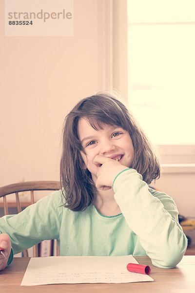 Porträt eines lächelnden kleinen Mädchens bei den Hausaufgaben