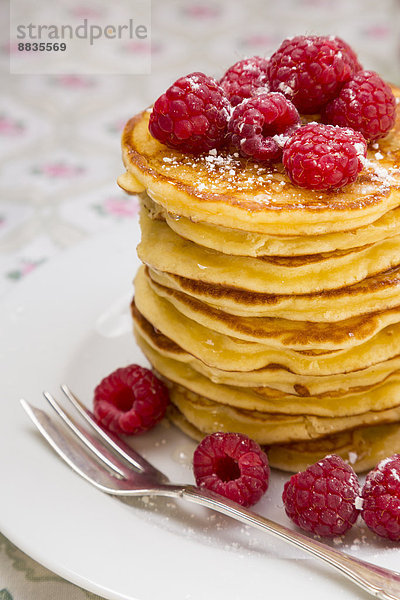 Stack of pancakes with honey  raspberries and icing sugar