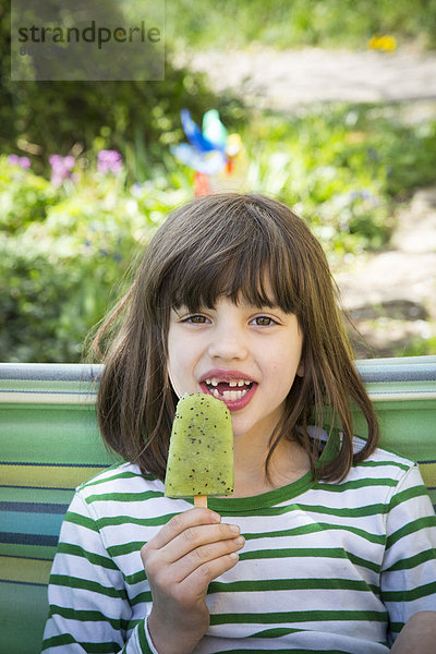 Porträt eines Mädchens mit Zahnlücke  das Kiwi-Eis-Lolly hält