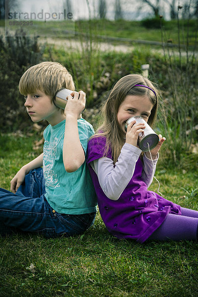 Junge und Mädchen spielen mit Blechdosentelefonen