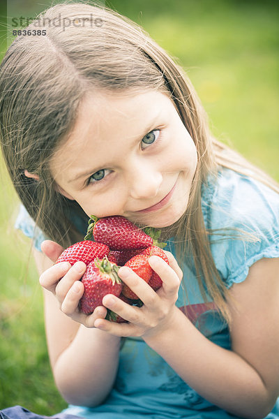 Porträt eines lächelnden kleinen Mädchens mit einer Handvoll Erdbeeren