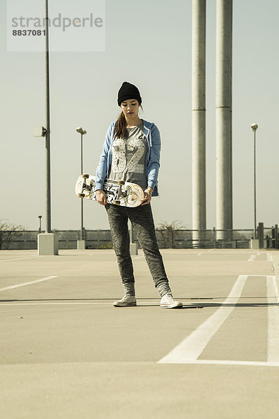 Junge Frau mit Skateboard auf Parkebene