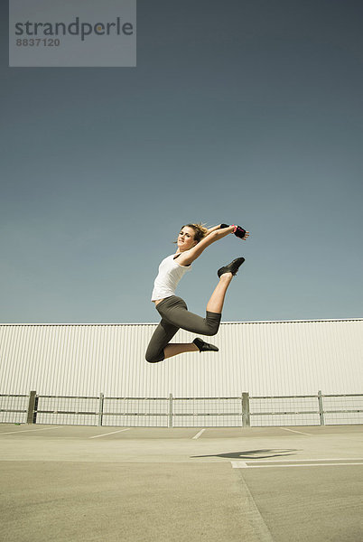 Junge Frau springt in der Luft auf Parkebene