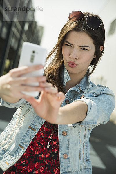 Grimassierende junge Frau  die mit einem Selfie nach draußen geht.